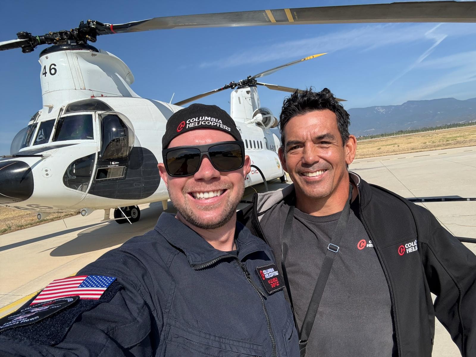 Two men posing by helicopters on a tarmac